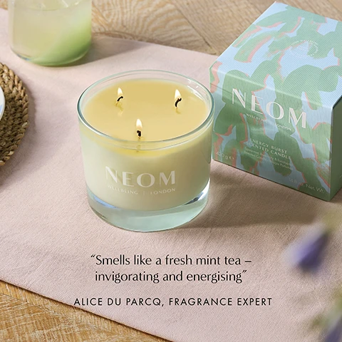 Image 1 - A lit three-wick NEOM candle and its patterned box are on a table, displaying the text NEOM WELLBEING LONDON NEOM WELLBEING LONDON ENERGY BURST SCENTED CANDLE 420ge 14.8 oz. Net. Wt. Smells like a fresh mint tea – invigorating and energising ALICE DU PARCQ, FRAGRANCE EXPERT. Image 2 - A large glass candle jar with a white candle inside and multiple wicks on a green background with text that reads STIMULATE THE SENSES AND SUPERPOWER YOUR DAY A potent blend of 6 pure essential oils 100% natural fragrances 100% naturally derived wax NEOM WELLBEING | LONDON.