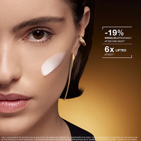 A close-up of a womans face features a white cream swatch on her cheek and gold earrings, with text displaying -19% WRINKLES APPEARANCE AFTER ONE NIGHT* 6X LIFTED EFFECT** *SELF-ASSESSMENT BY SCORING ON 32 SUBJECTS, ON WRINKLES VISIBILITY OF UNDERNEATH EYE AREA **SELF-ASSESSMENT BY SCORING ON THE EVOLUTION OF THE PRODUCT’S PERFORMANCES. COMPARISON BETWEEN THE EFFECT AFTER APPLICATION ON 34 WOMENS. THE EFFECT AFTER 1 MONTH ON 33 WOMEN.