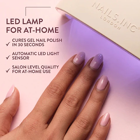 Image 1 - A hand with light pink and lavender gel nails is placed under a white LED nail lamp emitting purple light, with text that reads LED LAMP FOR AT-HOME, CURES GEL NAIL POLISH IN 30 SECONDS, AUTOMATIC LED LIGHT SENSOR, SALON LEVEL QUALITY FOR AT-HOME USE, and the brand name NAILS.INC LONDON on the lamp. Image 2 - Alt text generation failed